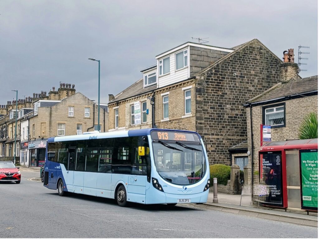 A bus at a bus stop with houses in the background