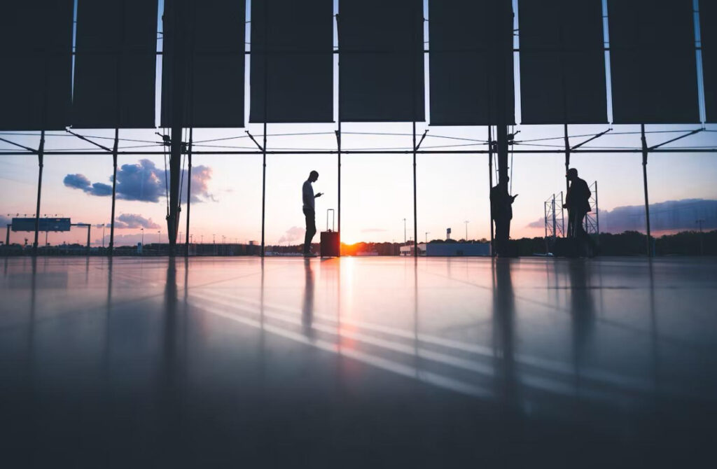Three silhouettes standing against sunset with suitcases in an airport lounge