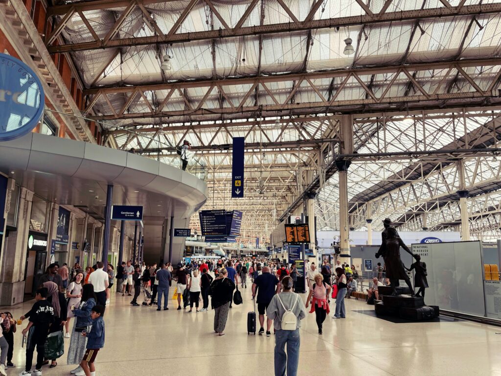 Lots of people with suitcases and bags walking across a station concourse