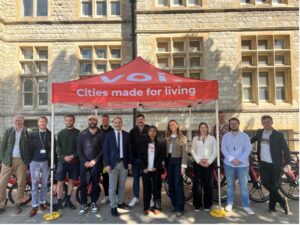 A group of people standing smiling at the camera, under a red gazebo with the words 'Voi - cities made for living'